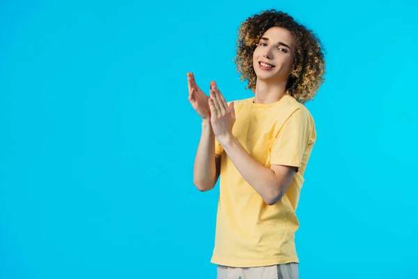 Smiling curly teenager applauding isolated on blue — Stock Photo