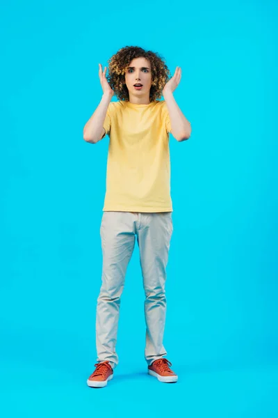 Adolescente encaracolado assustado com as mãos perto da cabeça isolado em azul — Fotografia de Stock