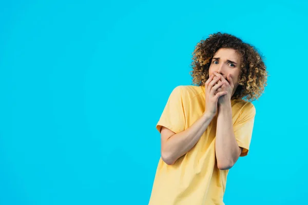 Scared curly teenager covering mouth with hands isolated on blue — Stock Photo