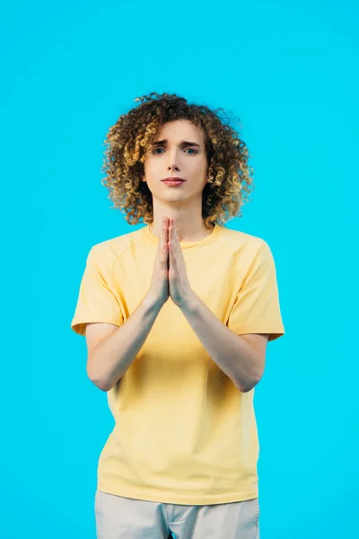 Кудрявый подросток с молитвенными руками, изолированными на голубом — стоковое фото