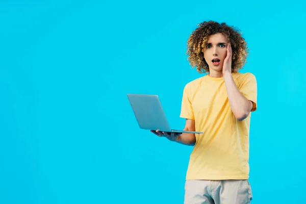 Estudante encaracolado chocado usando laptop isolado em azul — Fotografia de Stock