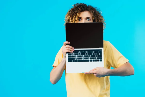 Verängstigte lockige Studentin versteckt sich hinter Laptop mit leerem Bildschirm isoliert auf blau — Stockfoto