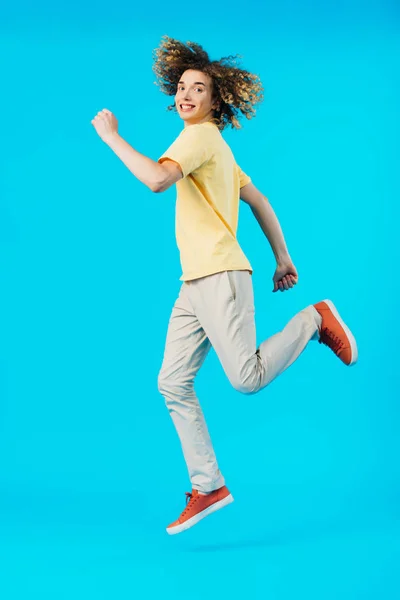 Feliz adolescente encaracolado pulando isolado no azul — Fotografia de Stock