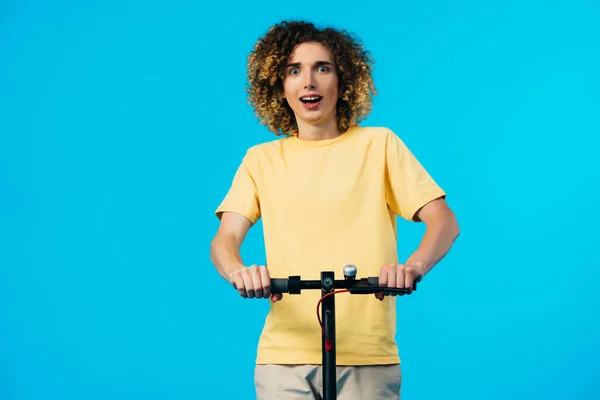 Excitado adolescente rizado montar scooter eléctrico aislado en azul - foto de stock