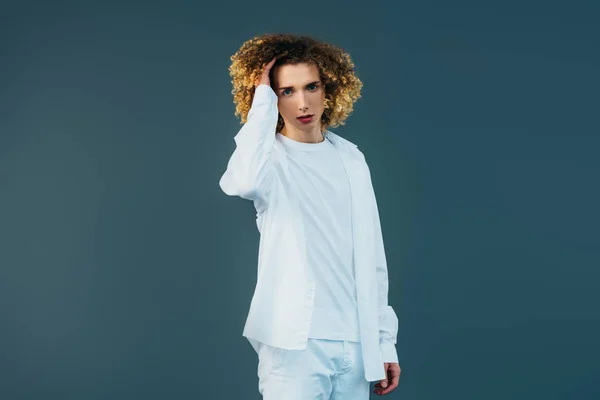 Curly teenager in total white outfit touching hair isolated on green — Stock Photo