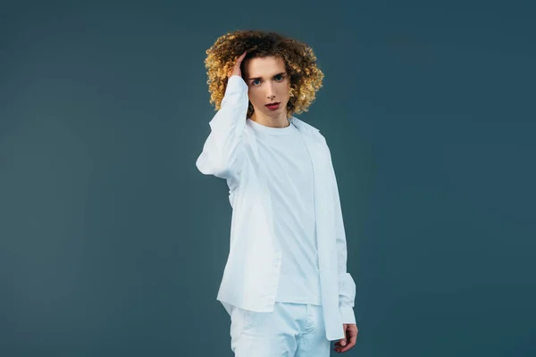 Adolescent bouclé en tenue blanche totale touchant les cheveux isolés sur vert — Photo de stock