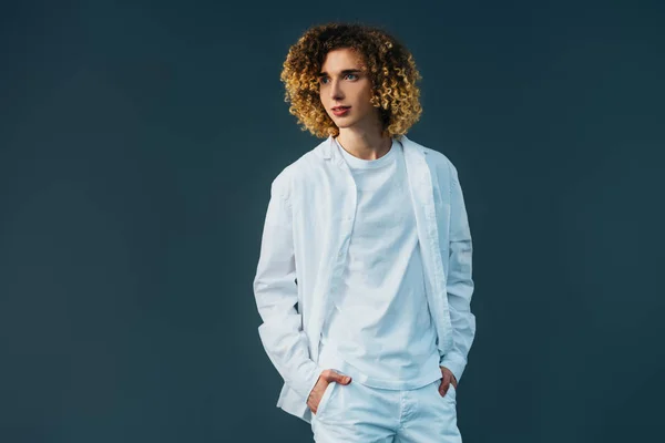 Curly teenager in total white outfit with hands in pockets looking away isolated on green — Stock Photo