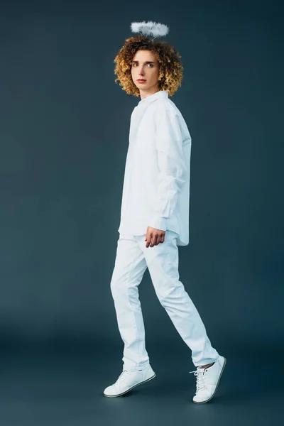 Full length view of curly teenager in angel costume with halo above head on green — Stock Photo
