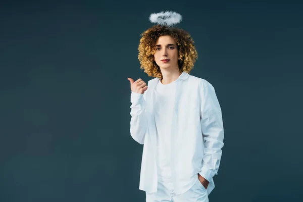 Curly teenager in angel costume with halo above head showing thumb up isolated on green — Stock Photo