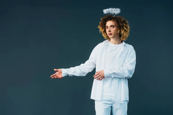 Curly teenager in angel costume with halo above head pointing with hand isolated on green — Stock Photo