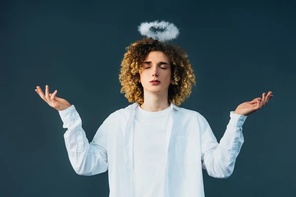 Adolescente riccio in costume da angelo con aureola sopra la testa, occhi chiusi e mani tese isolate sul verde — Foto stock