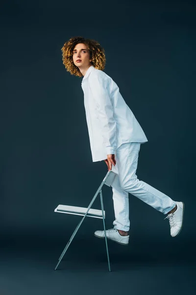 Adolescent bouclé élégant en tenue blanche totale debout sur la chaise sur vert — Photo de stock