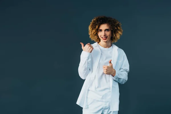 Sorrindo adolescente encaracolado elegante em roupa branca total mostrando polegares isolados no verde — Fotografia de Stock