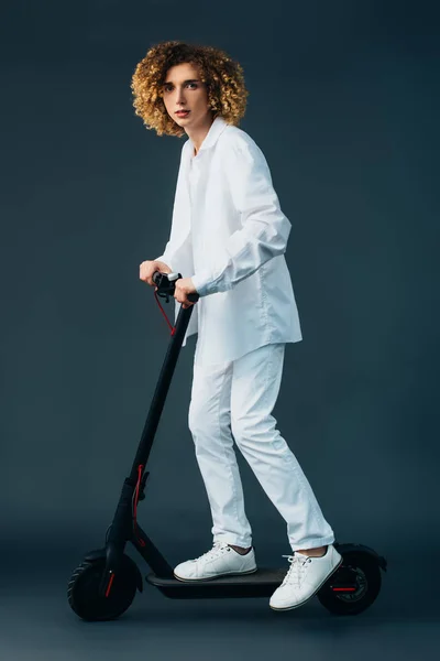 Elegante adolescente riccio in total white vestito cavalcando scooter elettrico sul verde — Foto stock