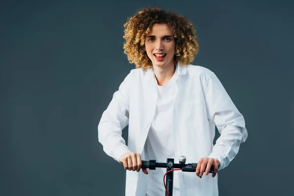 Sourire élégant adolescent bouclé en tenue blanche totale équitation scooter électrique isolé sur vert — Photo de stock