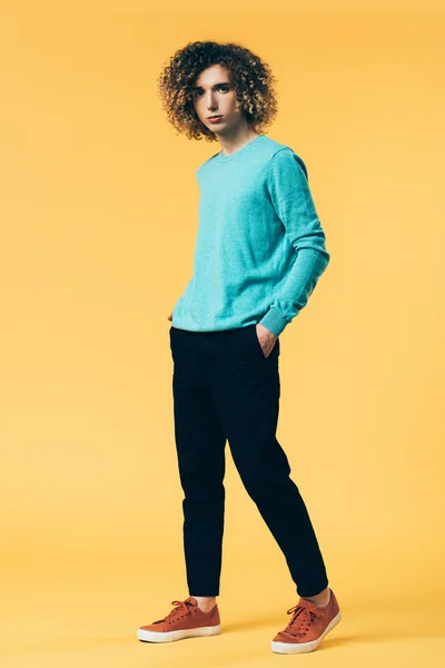 Curly teenager with hands in pockets on yellow background — Stock Photo