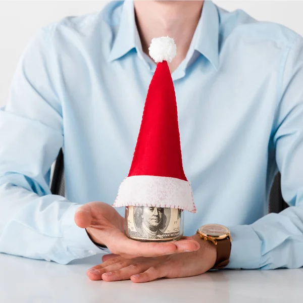 Vista ritagliata dell'uomo che tiene il vaso con le banconote del dollaro e il cappello di Babbo Natale isolato su bianco — Foto stock