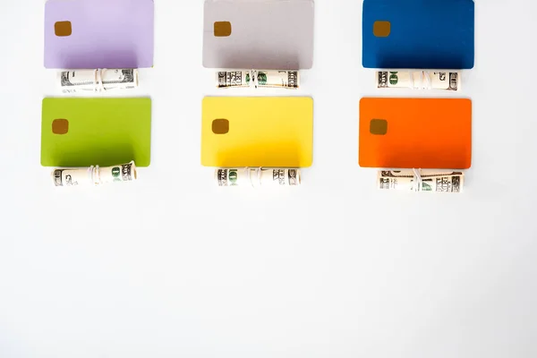 Vista dall'alto di modelli di carte di credito colorate vicino a rotoli di contante con banconote in dollari isolate su bianco — Foto stock