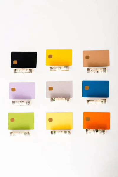 Vista dall'alto di modelli di carte di credito multicolore vicino a rotoli di contante con banconote in dollari isolate su bianco — Foto stock