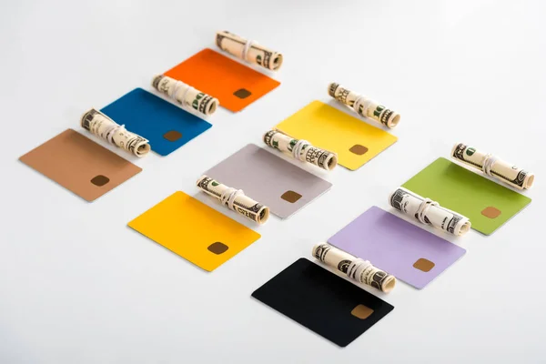 Modèles de cartes de crédit multicolores près de rouleaux de trésorerie avec des billets en dollars isolés sur blanc — Photo de stock
