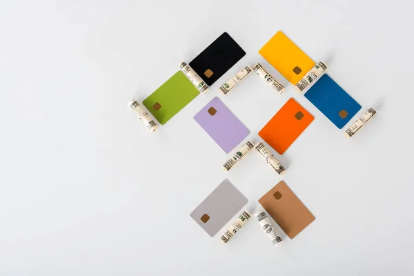Flat lay with multicolored credit card templates near cash rolls on white — Stock Photo