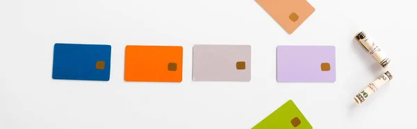 Panoramic shot of colorful credit card templates and cash rolls on white — Stock Photo