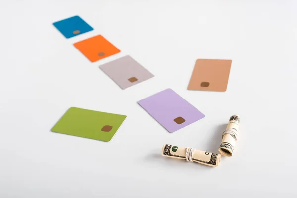 Selective focus of colorful credit card templates and cash rolls on white — Stock Photo