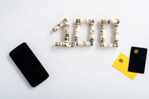 Vista superior del teléfono inteligente con pantalla en blanco cerca de rollos de efectivo y plantillas de tarjetas de crédito en blanco - foto de stock