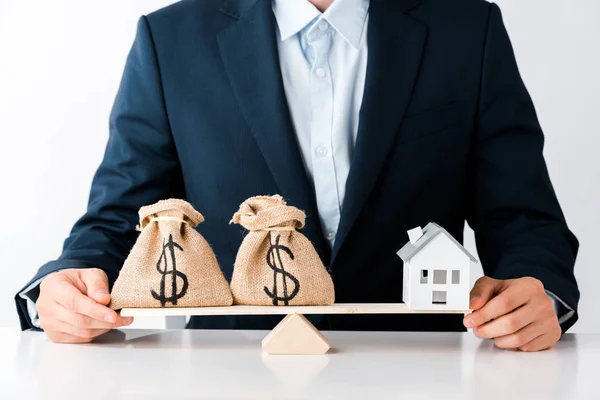 Vue recadrée de l'homme d'affaires près des balances avec des sacs d'argent et une maison en carton isolé sur blanc — Photo de stock