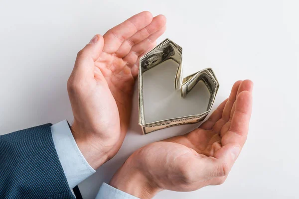 Vista superior del hombre de negocios cerca de billetes de dólar en forma de corazón en blanco - foto de stock