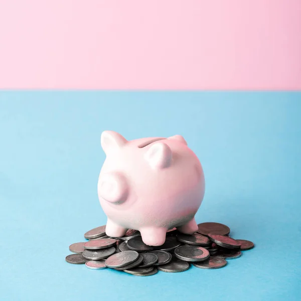 Fechar-se de moedas perto de banco porquinho isolado em azul e rosa — Fotografia de Stock