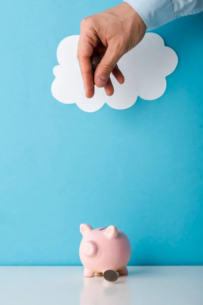 Vista cortada do homem jogando moeda perto de rosa porquinho banco em azul — Fotografia de Stock