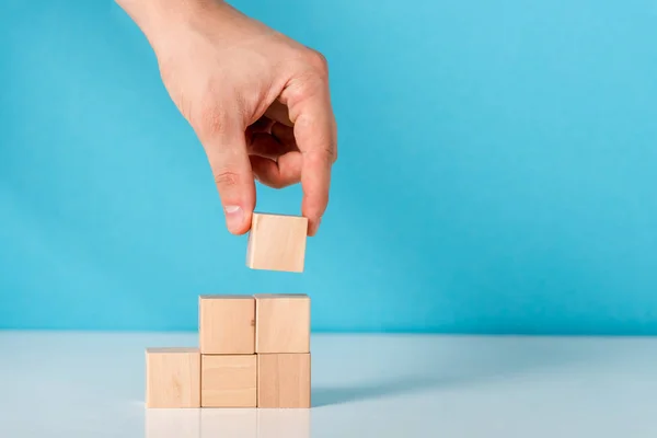 Cropped view of man putting wooden cube on blue — Stock Photo