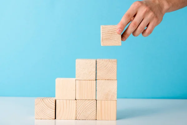 Vista ritagliata di uomo d'affari mettendo cubo di legno su blu — Foto stock