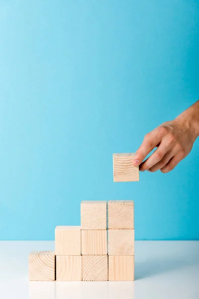 Vista ritagliata di uomo mettendo cubo di legno su blu con spazio copia — Foto stock