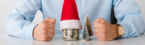 Panoramic shot of man with clenched fists near glass jar with money and santa hat isolated on white — Stock Photo