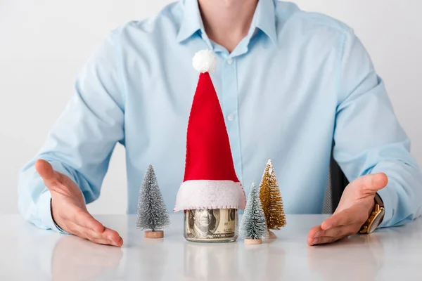 Abgeschnittene Ansicht eines Mannes mit Zeigen mit den Händen auf Glasgefäß mit Geld und Weihnachtsmütze isoliert auf weiß — Stockfoto