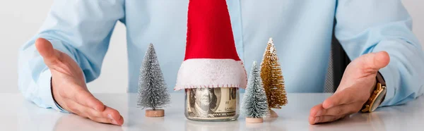 Panoramaaufnahme eines Mannes, der mit den Händen auf ein Glas mit Geld und Weihnachtsmütze zeigt, isoliert auf weiß — Stockfoto