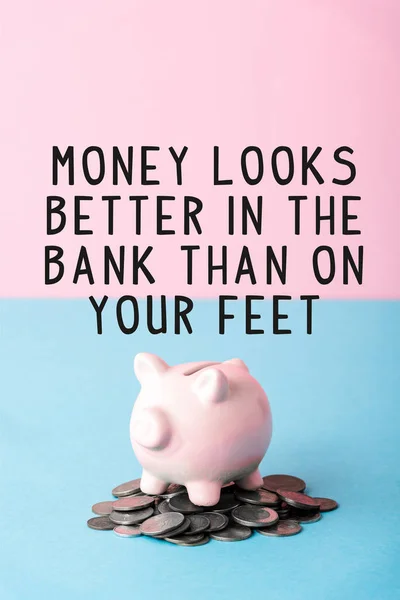 Monedas de plata cerca de alcancía y el dinero se ve mejor en el banco que en sus pies letras en azul y rosa - foto de stock