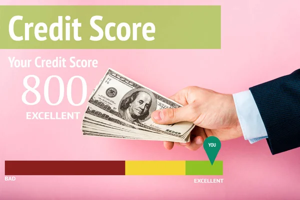 Vista recortada del hombre sosteniendo billetes de dólar en la mano cerca de letras de puntuación de crédito en rosa - foto de stock