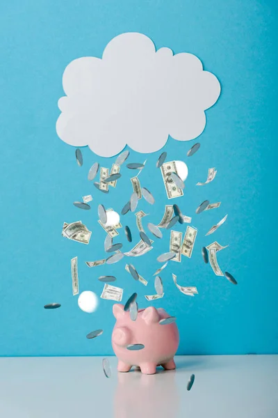 Рожевий скарбничка біля білої хмари і падаючі гроші на синій — стокове фото