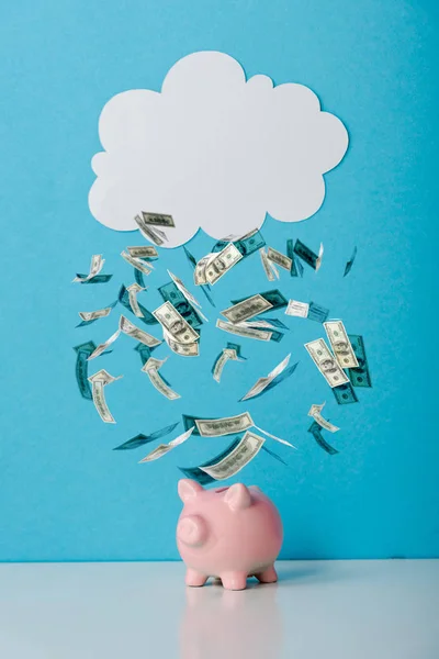 Pink piggy bank near white cloud and falling dollar banknotes on blue — Stock Photo