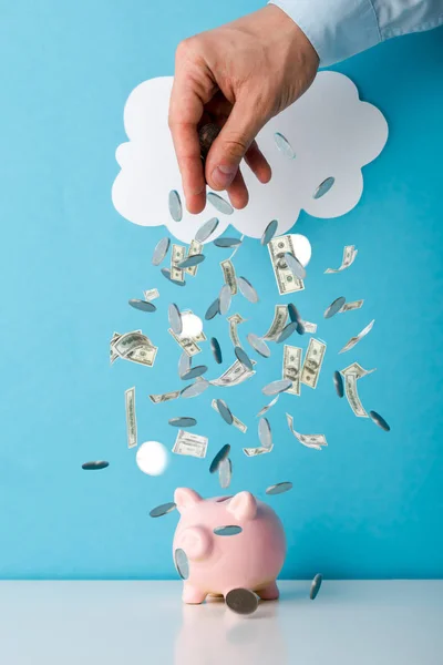 Cropped view of man throwing money near pink piggy bank on blue — Stock Photo