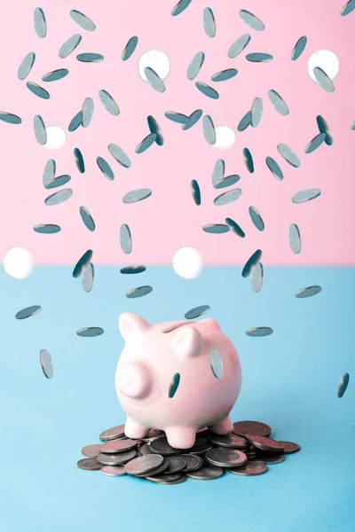 Falling silver coins near piggy bank on blue and pink — Stock Photo