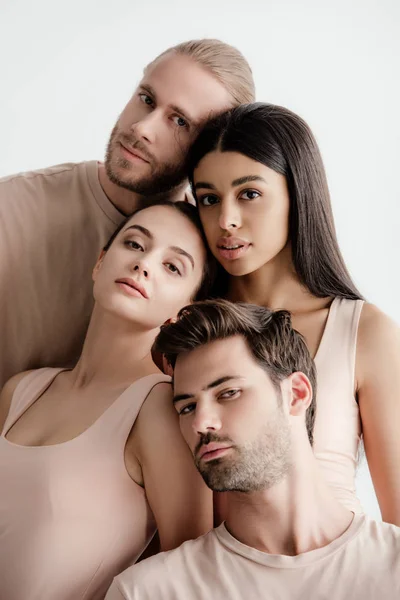 Jóvenes hombres y mujeres multiculturales en traje beige posando juntos aislados en blanco - foto de stock