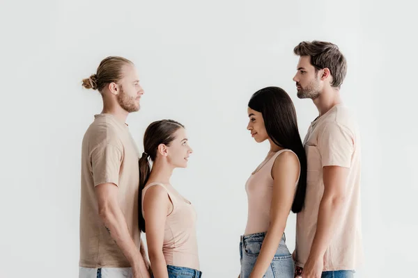 Vista lateral de homens e mulheres multiculturais jovens em roupa bege em pé face a face isolado em branco — Fotografia de Stock