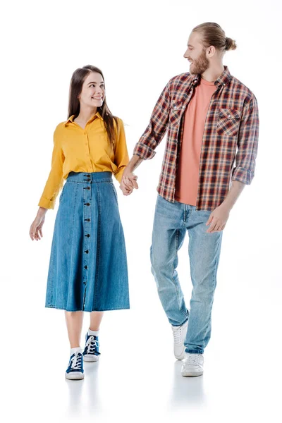 Full length view of happy young couple in casual outfit walking and holding hands isolated on white — Stock Photo