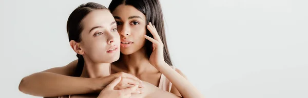 Hermosas chicas jóvenes multiculturales en traje beige tiernamente tocándose aislados en blanco, plano panorámico - foto de stock