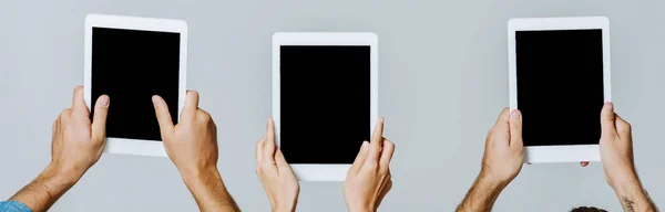 Vista recortada de jóvenes amigos sosteniendo tabletas digitales con pantallas en blanco aisladas en gris, plano panorámico - foto de stock