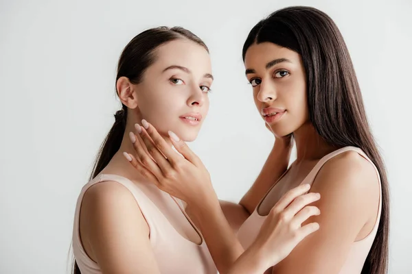 Beautiful young multicultural girls in beige outfit tenderly touching each other isolated on white — Stock Photo
